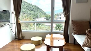 Una habitación con piso de madera, una mesa redonda, un sofá y una ventana que da a una ladera verde.