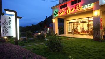 Un restaurante con un letrero iluminado y un jardín bien cuidado al frente.