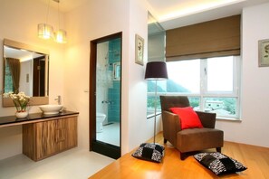 Relax in a stylish room with a comfortable armchair, glass-enclosed shower, and a vanity with a mirror.