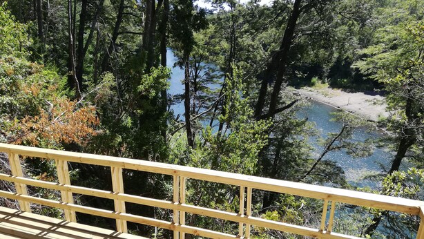 A wooden deck with a railing overlooking a forested area and a body of water. - Rustic Barn Cabin  (Pucon)