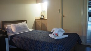 Habitació d'hotel amb un llit, una taula de nit, escriptori, làmpada, una paperera i una porta.