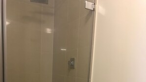 Cabina de ducha amb vidre, vàter blanc i barra per a tovalloles.