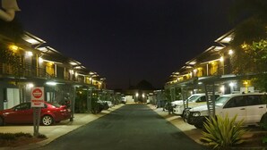 Zona d'aparcament de nit amb diversos cotxes aparcats per files, un senyalitzador de 'Prohibida la circulació, sentit contrari' i edificis amb finestres il·luminades.