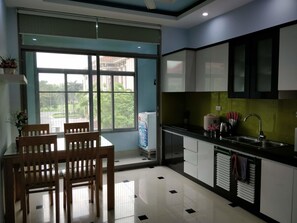 A modern kitchen with a dining area, large windows, and a view of greenery outside.