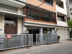 A multi-story residential building with a gated entrance, a balcony with metal railings, and a visible number 47 on the wall.