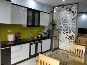 A modern kitchen with white cabinets, a black countertop, and a decorative partition. - Zody Apartment (Hanoi)