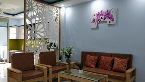 Uma área de recepção com um sofá castanho, duas cadeiras castanhas, uma mesa de centro com tampo de vidro e um painel branco decorativo.