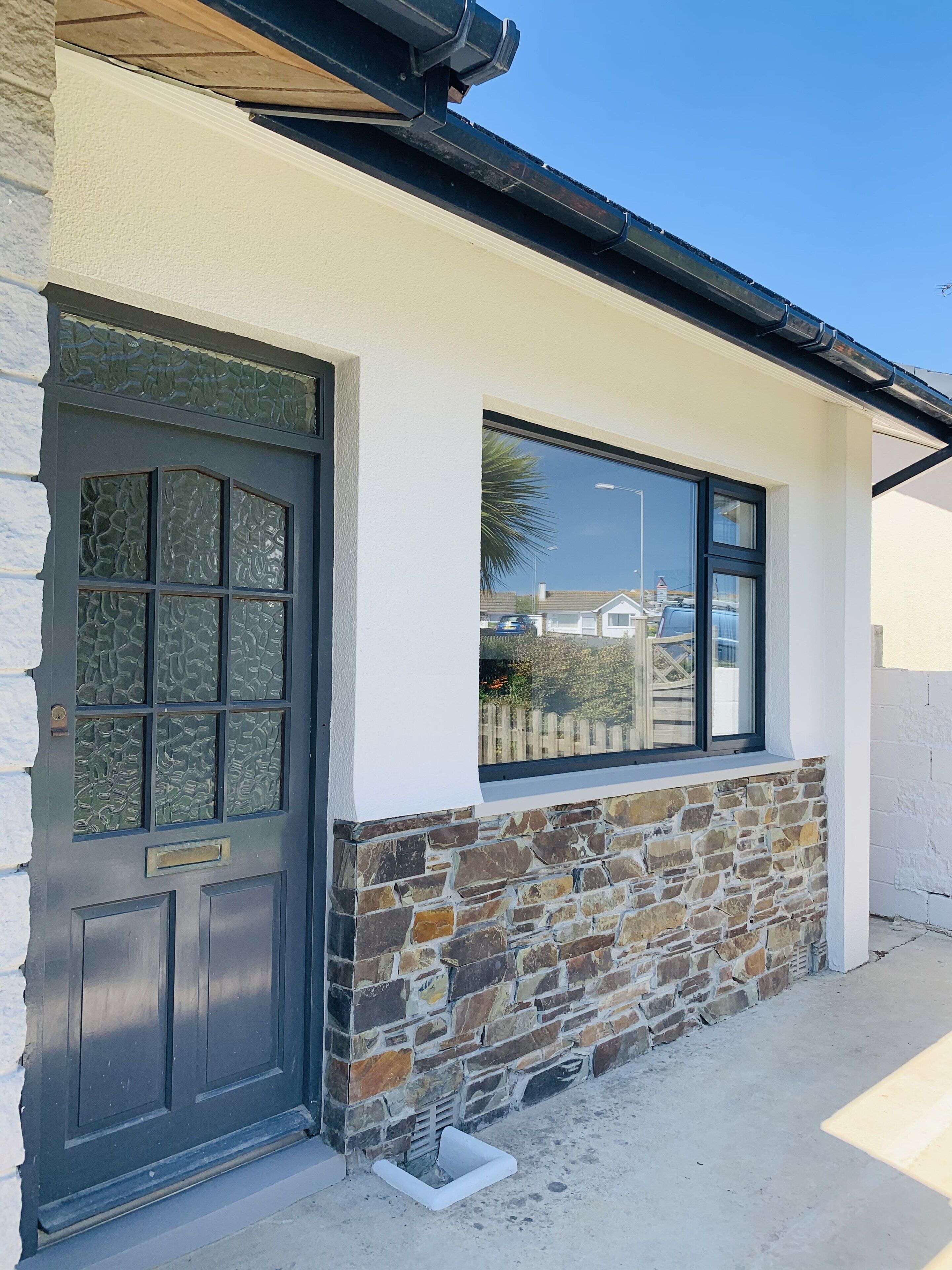 A building with a stone facade, a black door with glass panels, and a window with a view of the street.