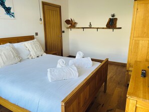 Una cama bien tendida con ropa blanca y toallas enrolladas, un cabecero de madera, un armario de madera y una estantería con adornos.