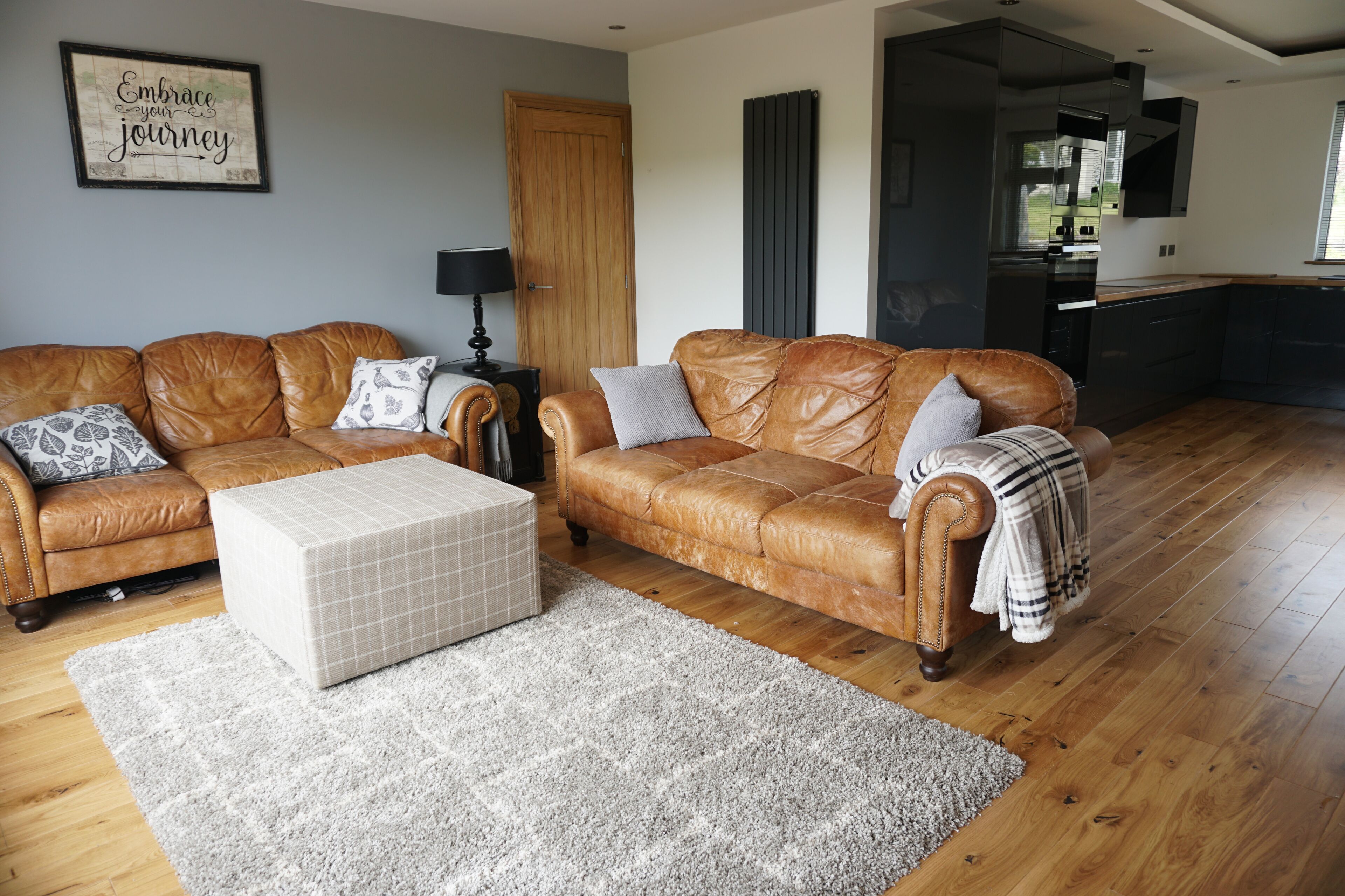 A living room with a brown leather sofa, a white ottoman, and a grey rug.