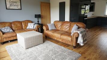 A living room with a brown leather sofa, a white ottoman, and a grey rug.