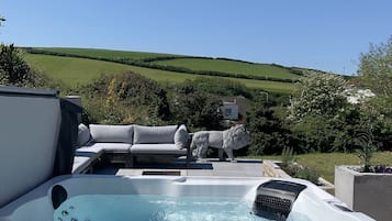 A hot tub with a lion statue, a white outdoor sofa, and a view of rolling hills.