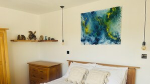 Una camera da letto con un letto, comodini in legno, una cassettiera, una mensola a parete con oggetti decorativi e un quadro.