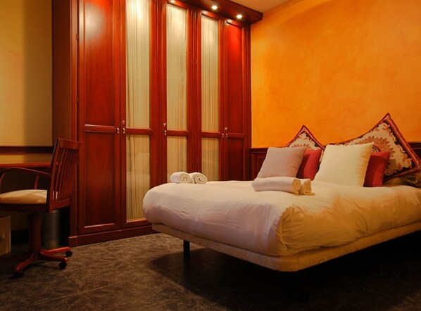 A hotel room with a large bed, a wooden wardrobe, a chair, and a desk.