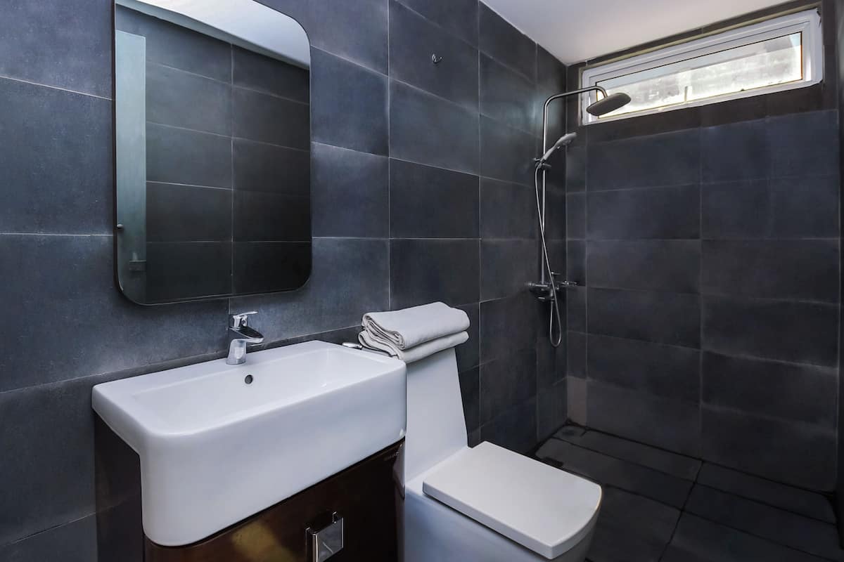 Un baño moderno con baldosas oscuras, un lavamanos blanco, un inodoro y una ducha.