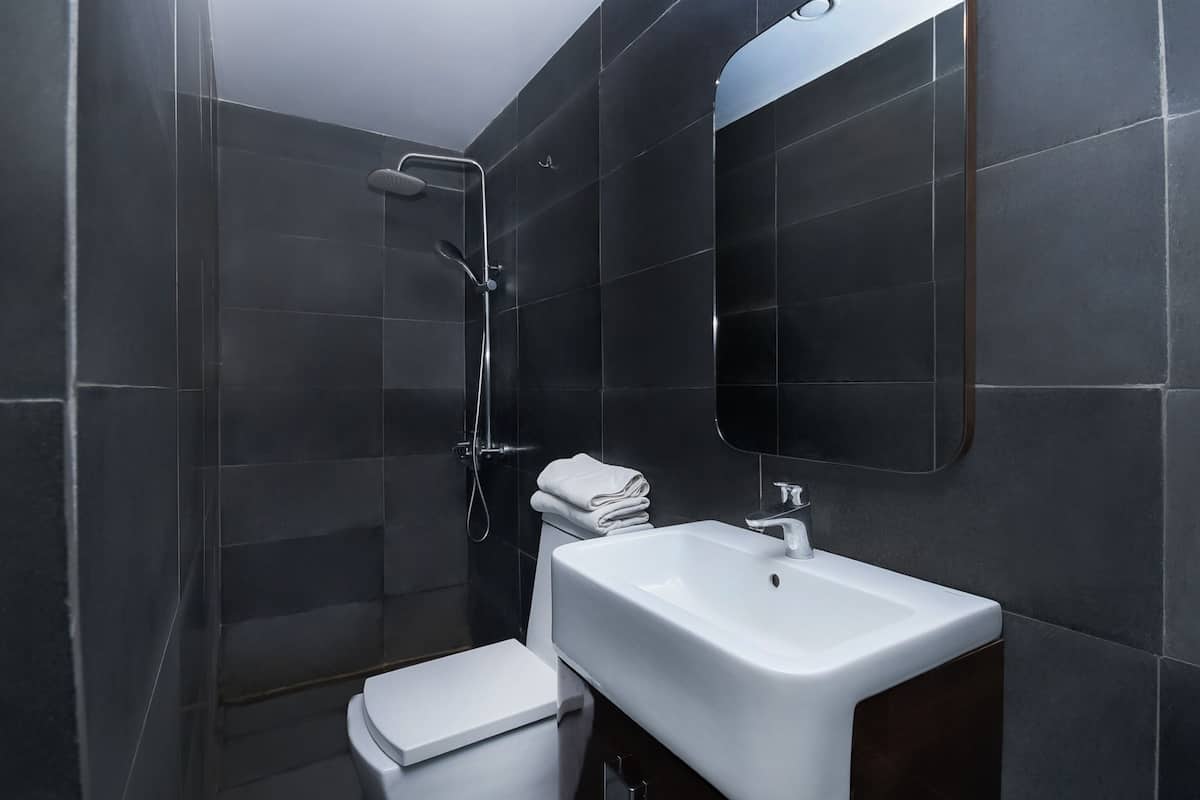 Un baño moderno con baldosas oscuras, un lavamanos blanco y una ducha.