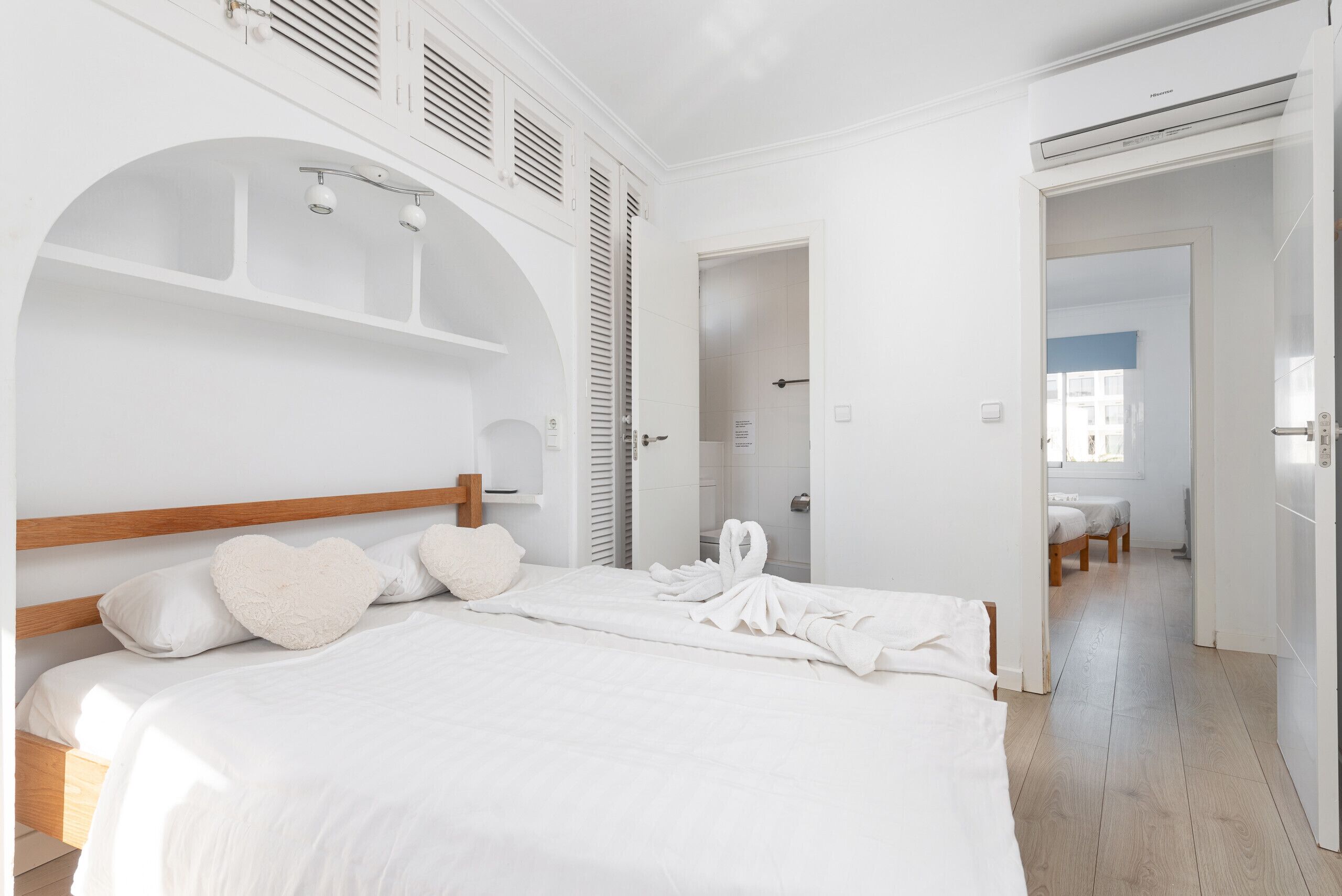 A modern hotel room with a large bed, a wooden headboard, and a white color scheme.