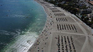 An aerial view of a beach with rows of umbrellas and sun loungers, a clear blue sea, and buildings in the background. - Apartment Thierry 10 m from the beach, 2 Swimmingpools, for 4 People (Alcúdia)