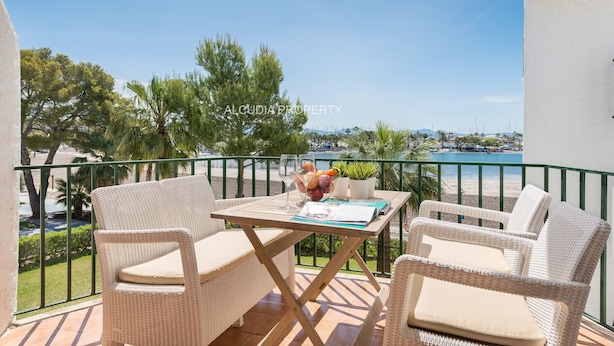 A balcony with wicker furniture, a table with a newspaper, and a view of the sea and boats. - Apartment Thierry 10 m from the beach, 2 Swimmingpools, for 4 People (Alcúdia)