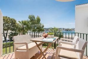 Un balcon agrémenté de meubles en osier, une table avec un journal et une vue sur la mer et les bateaux.