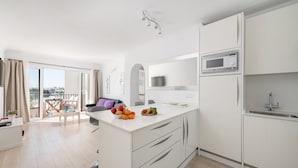 A modern kitchen with white cabinetry, a microwave, and a sink. There is a dining area with a table and chairs, and a balcony with a view. - Apartment Thierry 10 m from the beach, 2 Swimmingpools, for 4 People (Alcúdia)