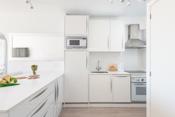 Une cuisine moderne avec des meubles blancs, un four à micro-ondes encastré, une hotte de cuisinière en acier inoxydable et un lave-vaisselle.