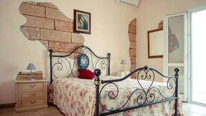 Een slaapkamer met een bed, nachtkastje, dressoir, muur met een bakstenen patroon, een fotolijst en een spiegel.