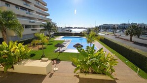 Un hotel con zona de piscina, que incluye sillas de descanso y sombrillas, rodeado de vegetación y un cielo despejado.