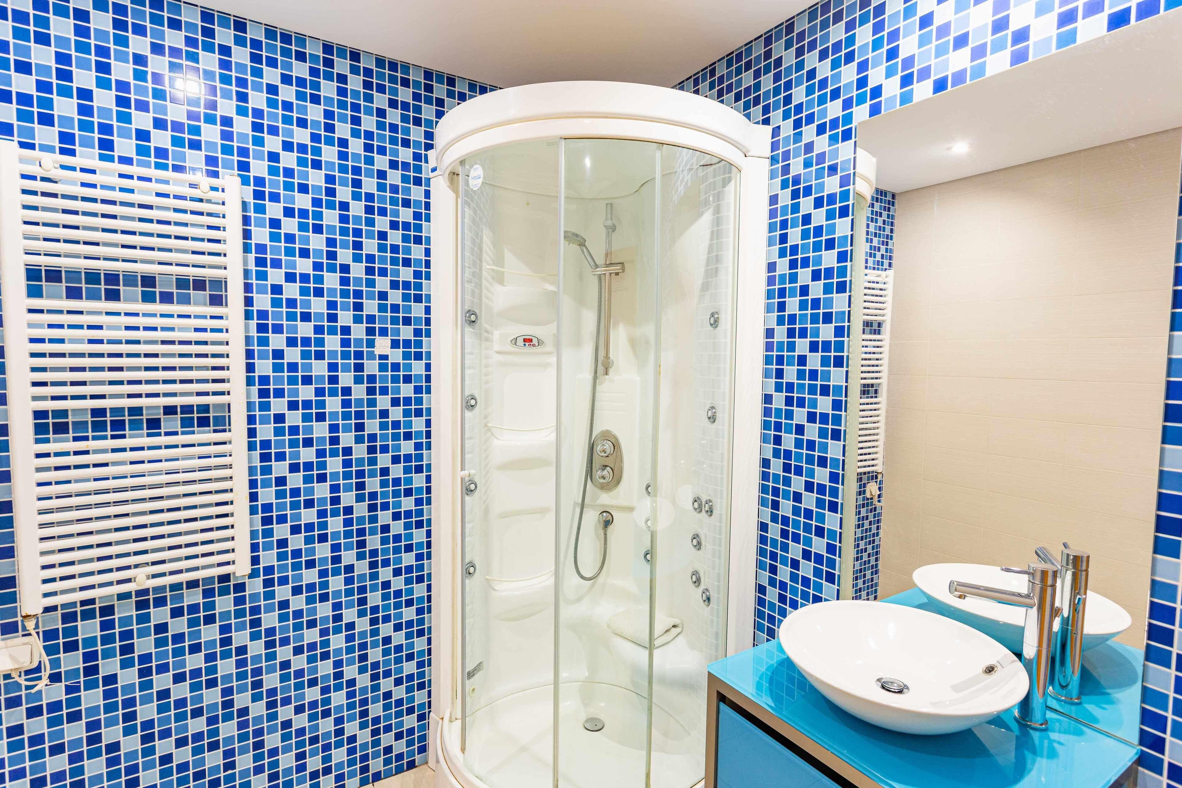 A bathroom with a glass-enclosed shower, a sink with a blue countertop, and blue mosaic tiles on the walls.