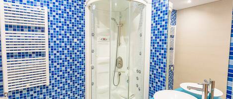 A bathroom with a glass-enclosed shower, a sink with a blue countertop, and blue mosaic tiles on the walls.