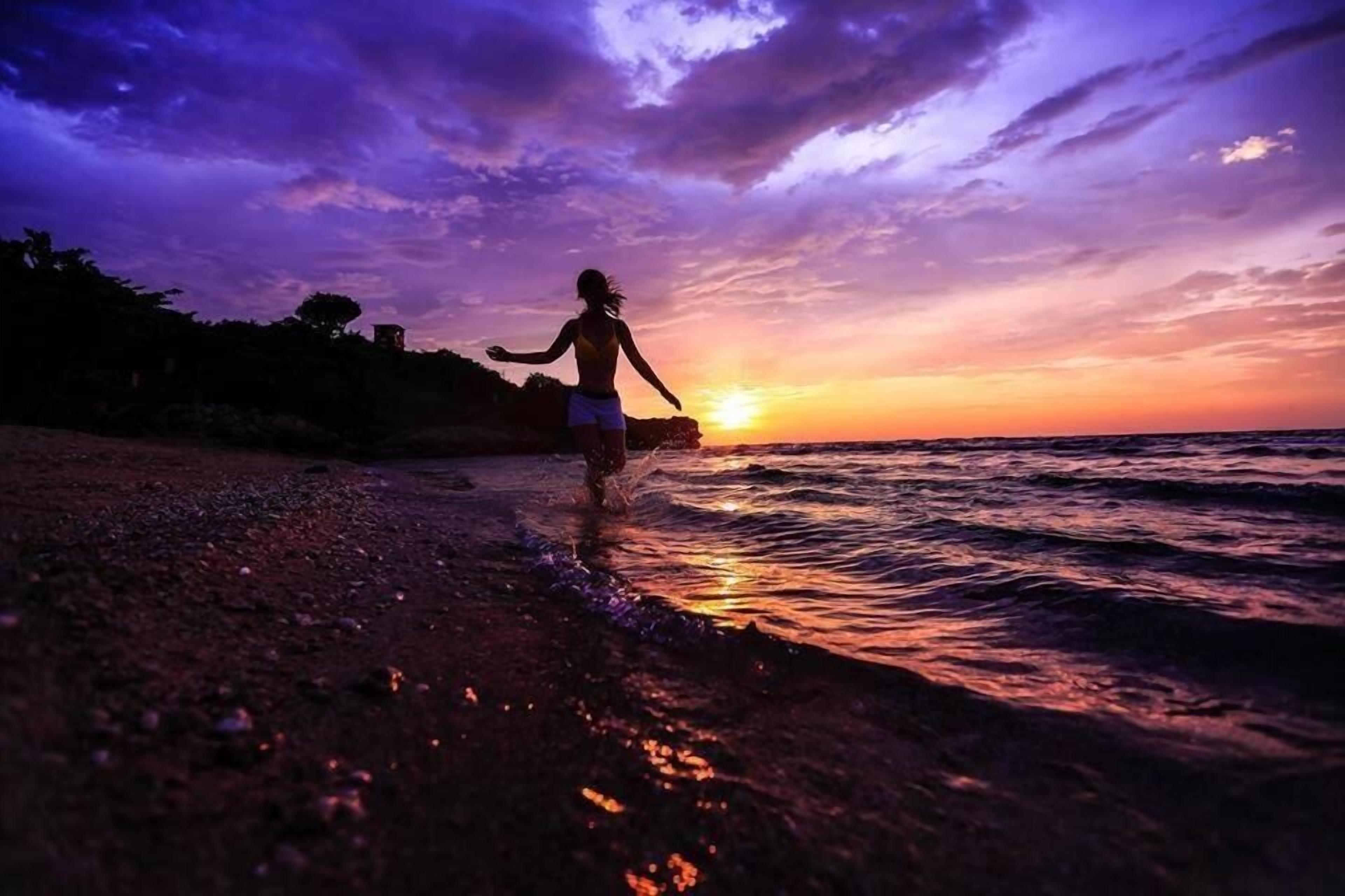 A silhouette of a person walking along a beach at sunset.