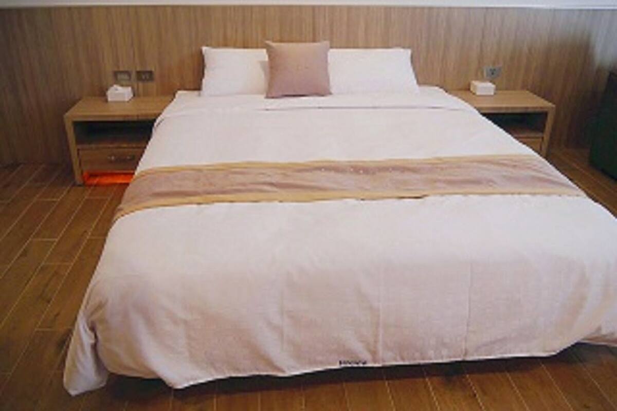 A hotel room with a large bed, wooden headboard, two bedside tables, and a nightstand.