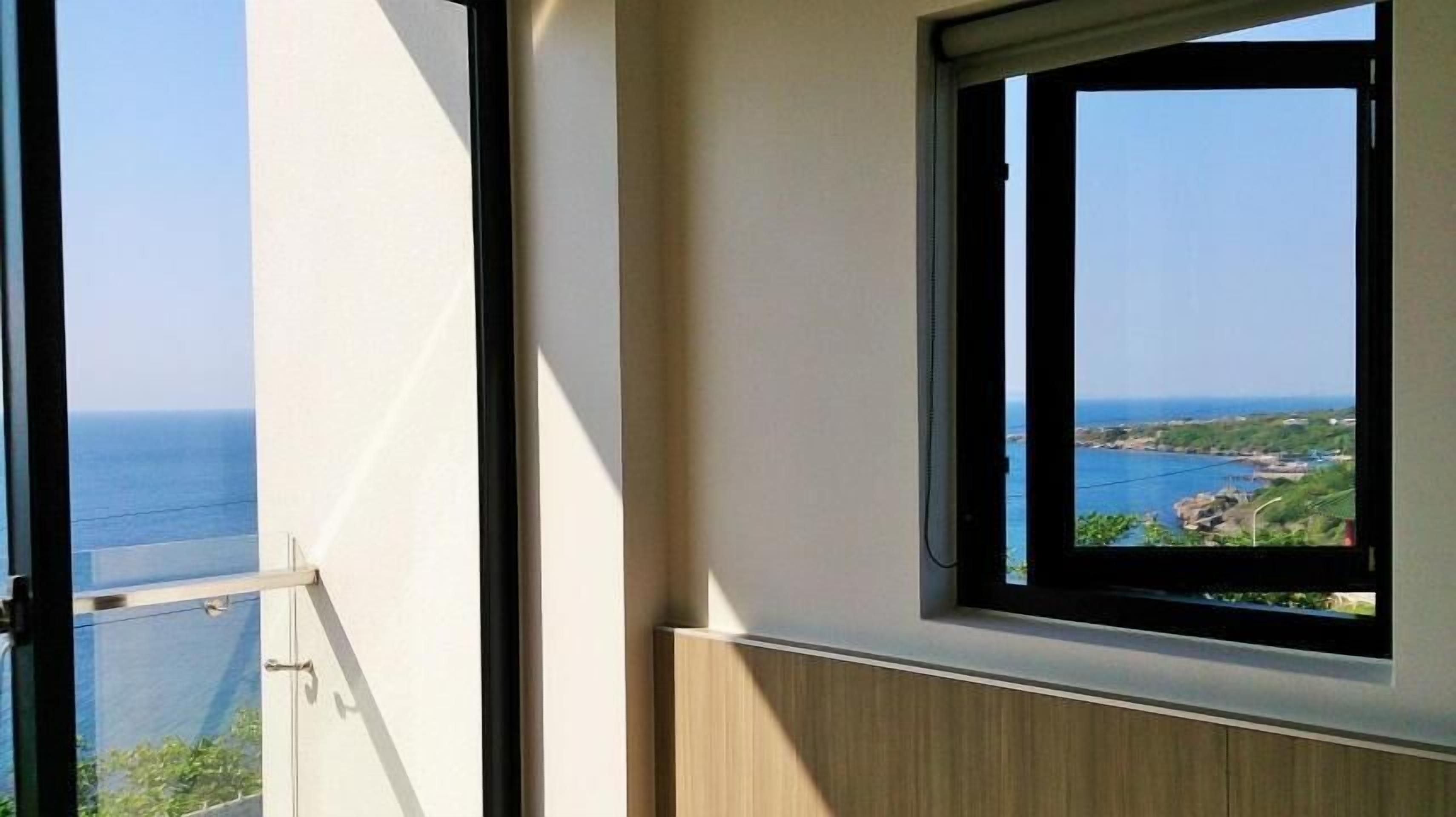 A room with a large window offering a view of the sea and a distant coastline.