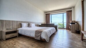 A modern hotel room with a large bed, a built-in bench, a small table, and a view of the outdoors. - Venice Seaview Hotel (Liuqiu)