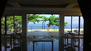 A restaurant with large windows offering a view of the sea and a tree. - Venice Seaview Hotel (Liuqiu)