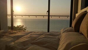 A bedroom with a large window overlooking a body of water at sunset. - Venice Seaview Hotel (Liuqiu)