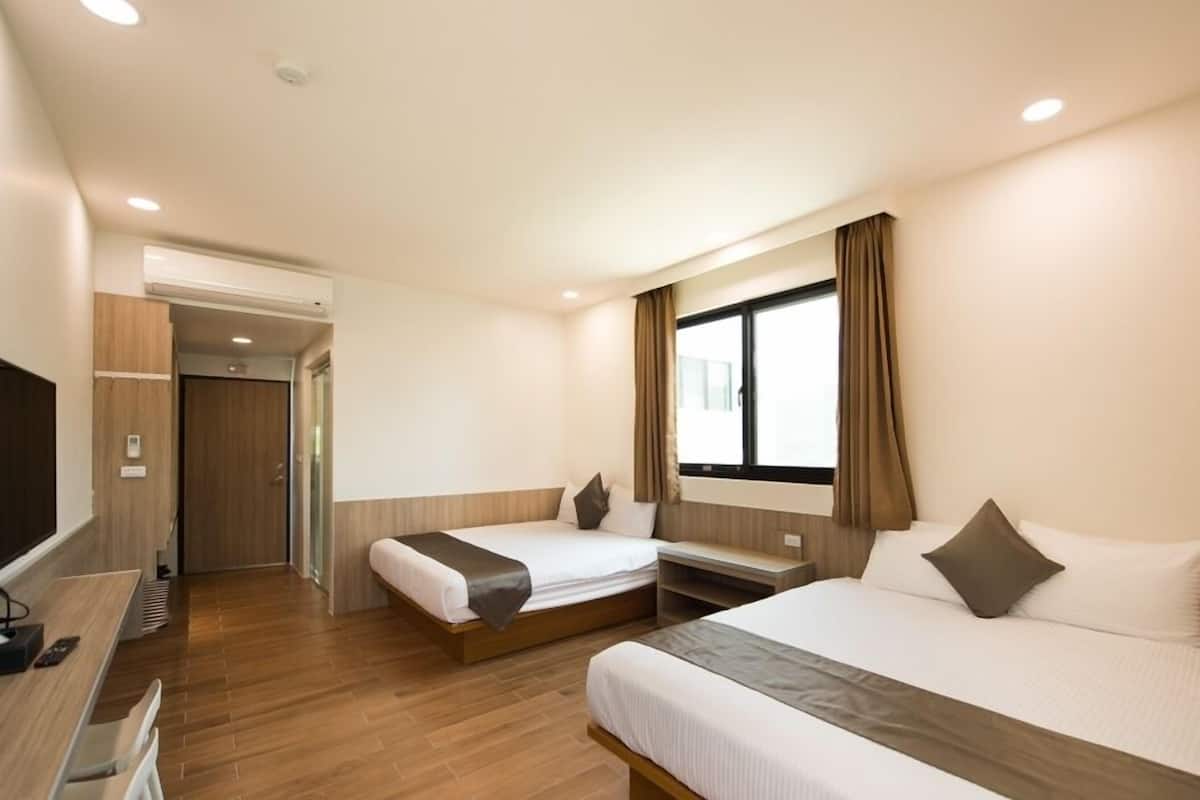 A hotel room with two beds, a desk, a TV, and a window with curtains.