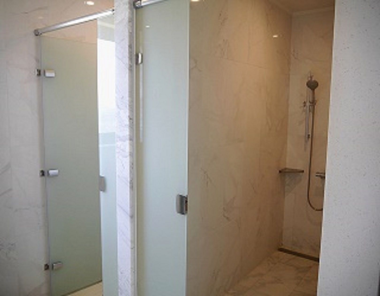 A glass-enclosed shower area with a handheld showerhead and a wall-mounted faucet.