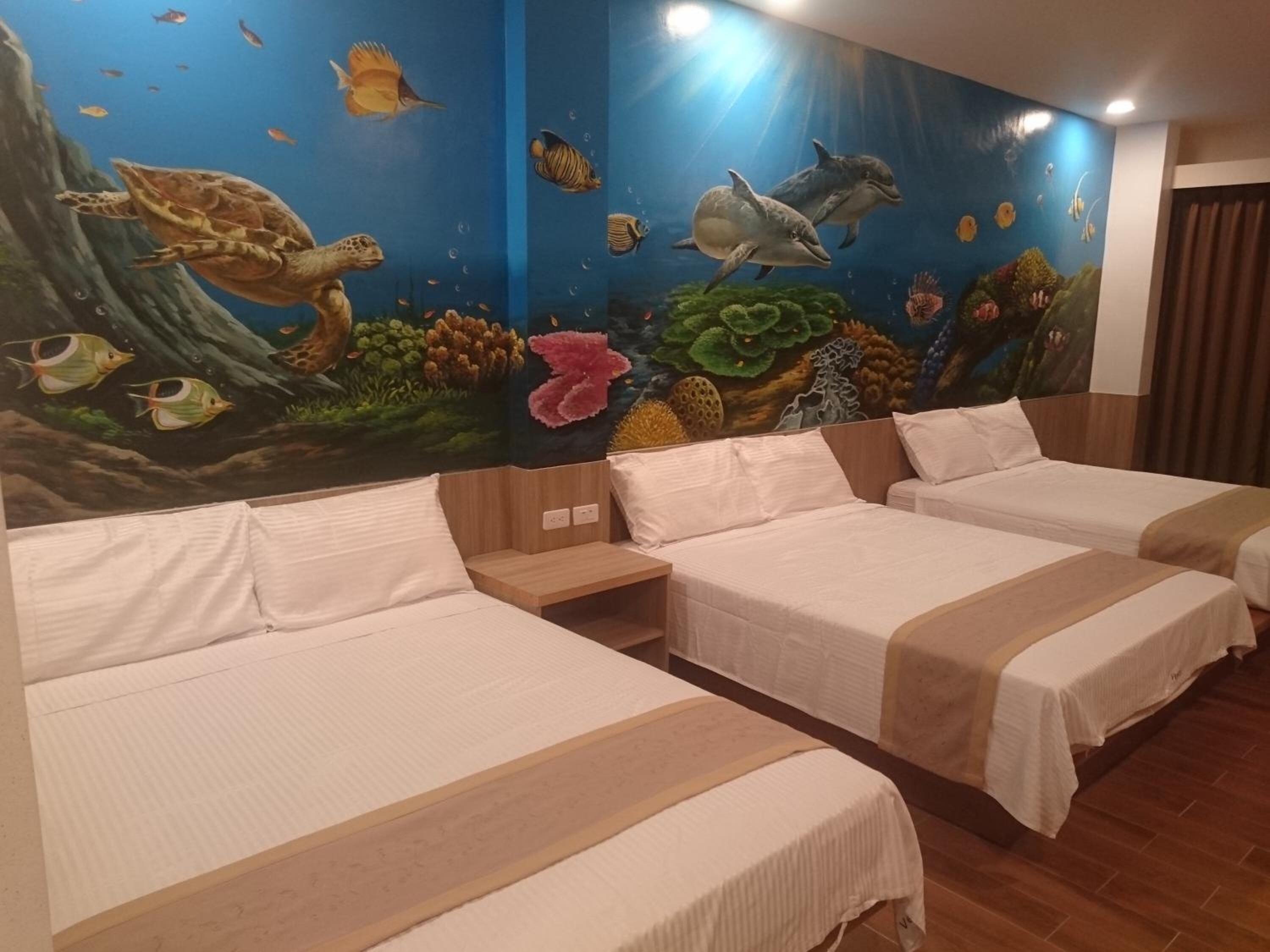 Una habitación de hotel con tres camas, un mural de vida marina en la pared y suelo de madera.