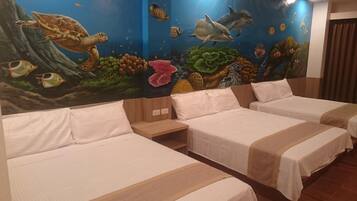 Una habitación de hotel con tres camas, un mural de vida marina en la pared y suelo de madera.