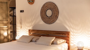 A neatly made bed with a wooden headboard, a wall-mounted circular decorative item, and a bedside table with a lamp. - House 34 - The Bougainvillea (Ceglie Messapica)