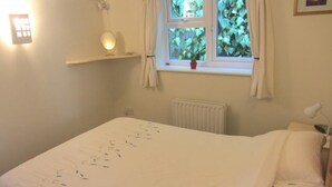 Una camera da letto con un letto, un comodino, una finestra con tende, un termosifone e una mensola a parete con una lampada.