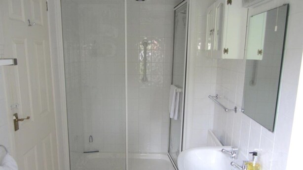 Un bagno con doccia vetrata, lavandino bianco con specchio e asciugamano appeso al muro.