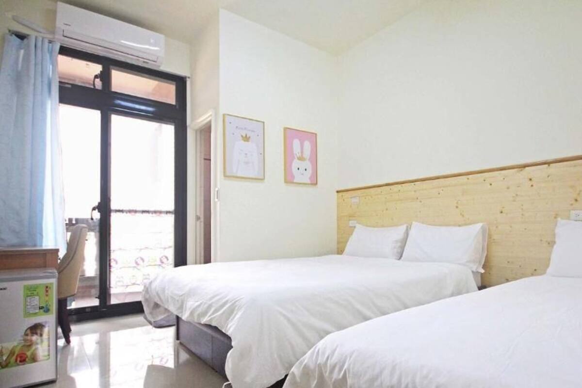 A hotel room with two beds, a wooden headboard, a window with a view, and a small table with a refrigerator.