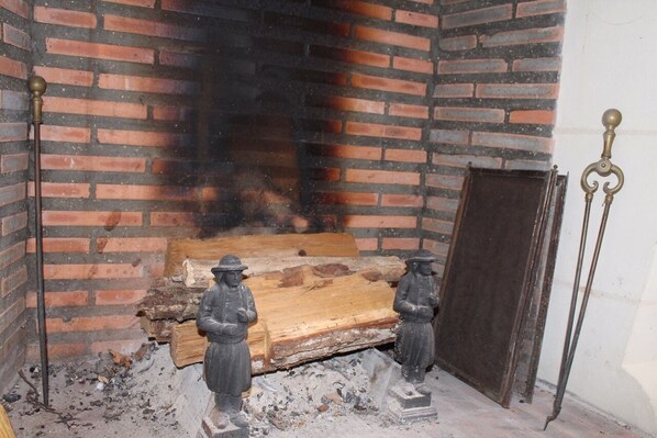 A brick fireplace with two statues on either side, a wooden log, and a metal door.