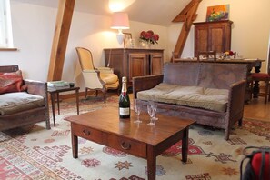 A cozy living room with a wooden coffee table, a sofa, and a chair. A bottle of champagne and two glasses are on the table.