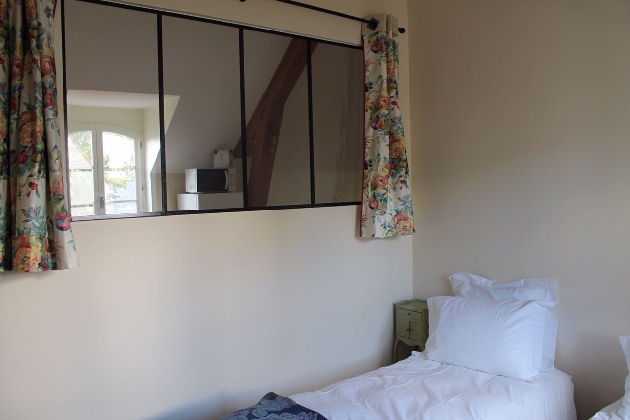 A bedroom with a bed, a nightstand, a mirror, and a window with curtains.