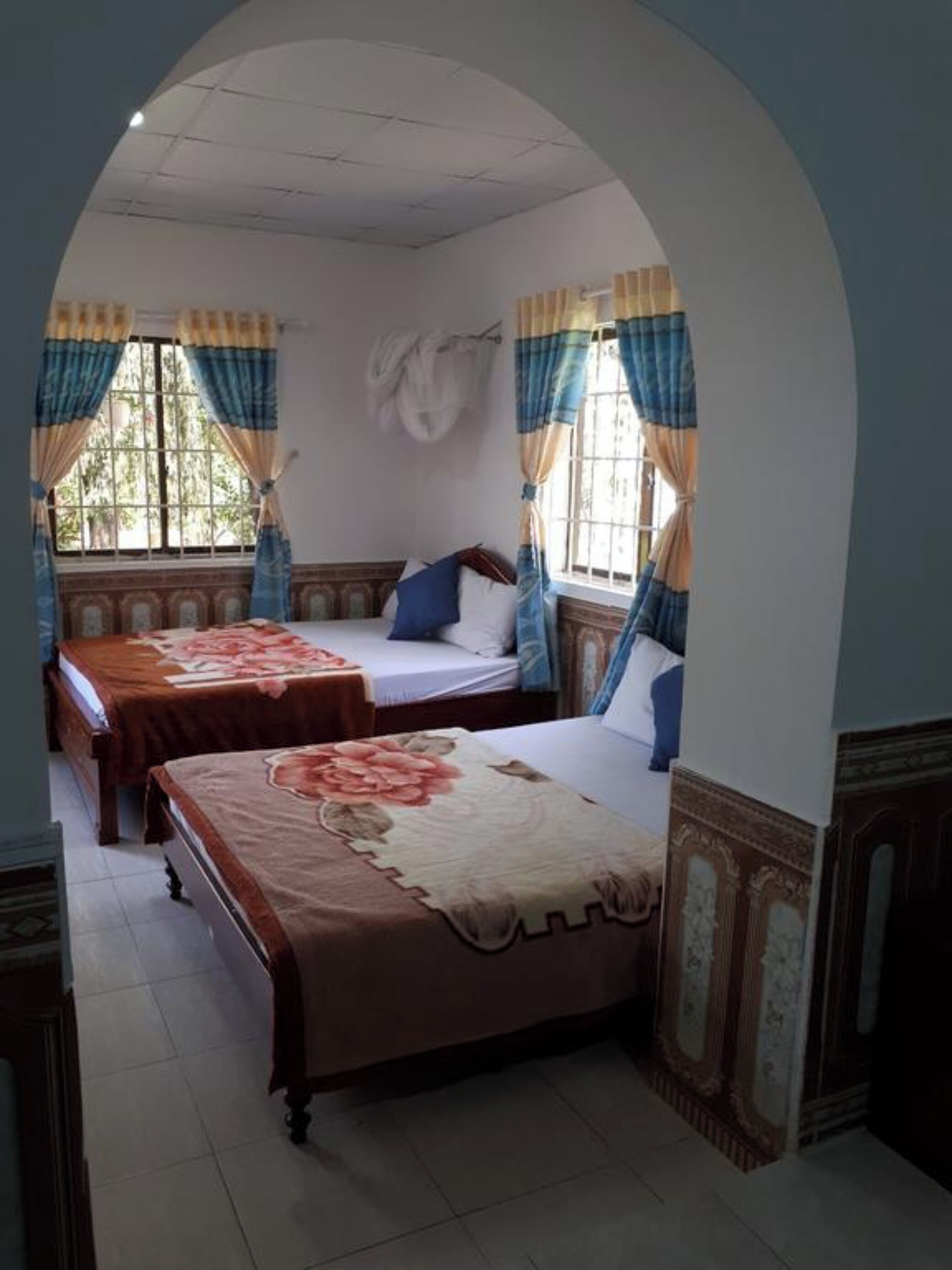 A room with two beds, a window with curtains, and an arched doorway.