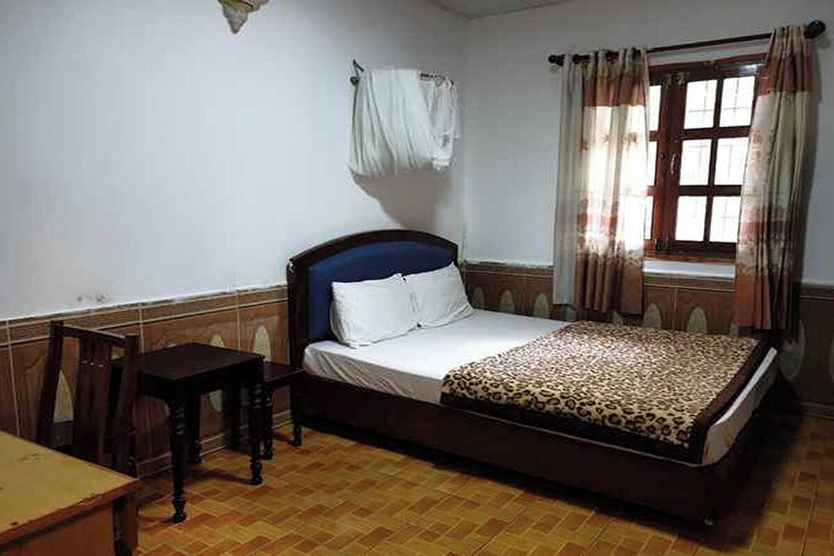 Une chambre à coucher comprenant un lit, une petite table, une fenêtre avec des rideaux et un porte-serviettes fixé au mur.