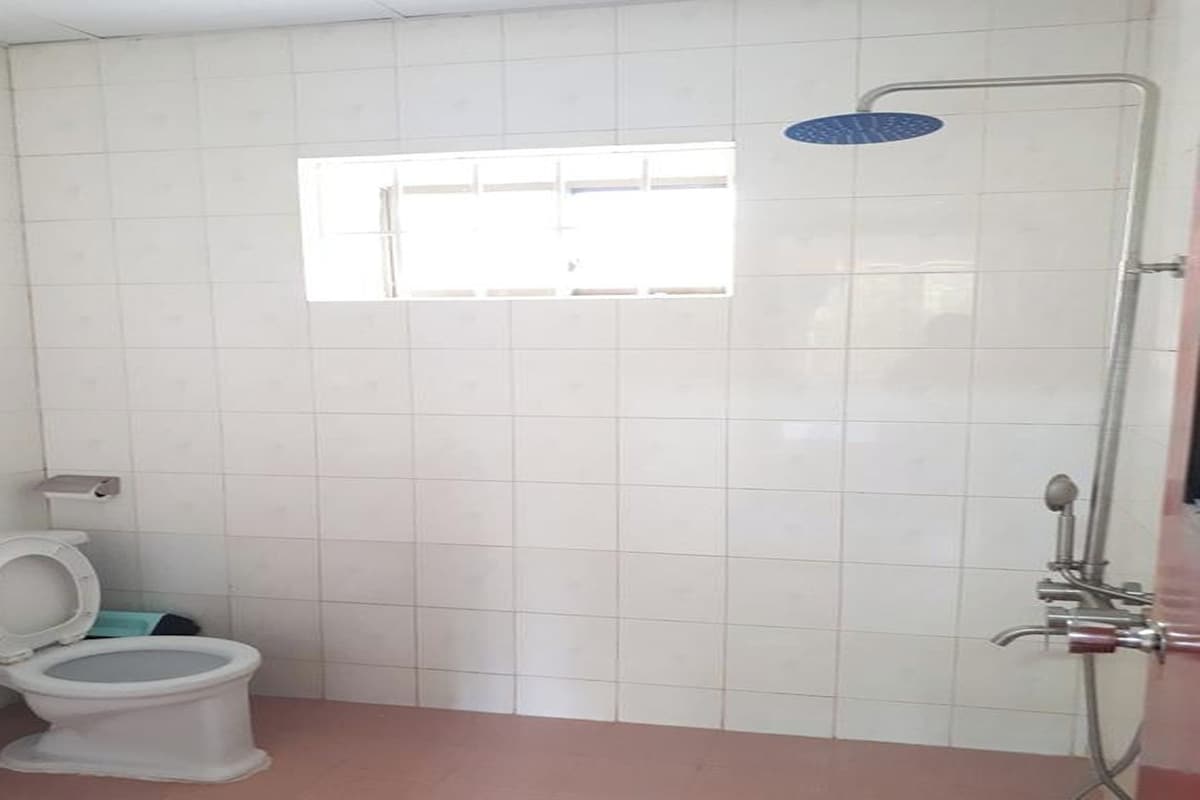 A bathroom with white tiled walls, a window, a toilet, and a shower.